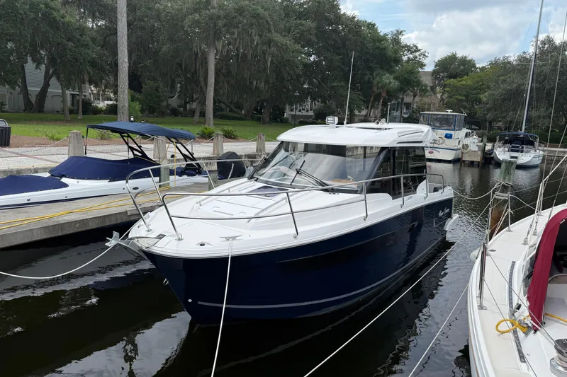The Image of 2020 Jeanneau NC 895 boat docked in a marina, surrounded by trees and other boats. - 0