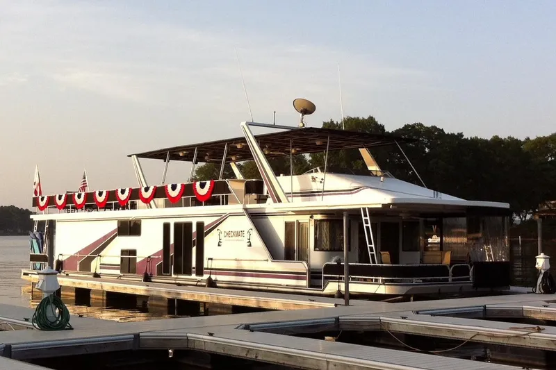 The Image of 1998 Sumerset 16x80 houseboat docked, decorated with patriotic bunting, under a clear sky. - 0