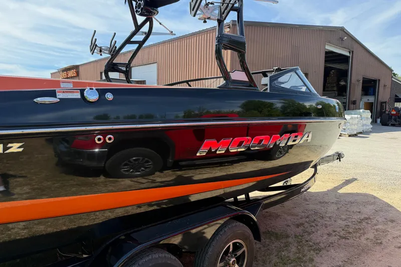 Slide: The Image of 2019 Moomba Craz boat with sleek black and orange design near a warehouse. - 2