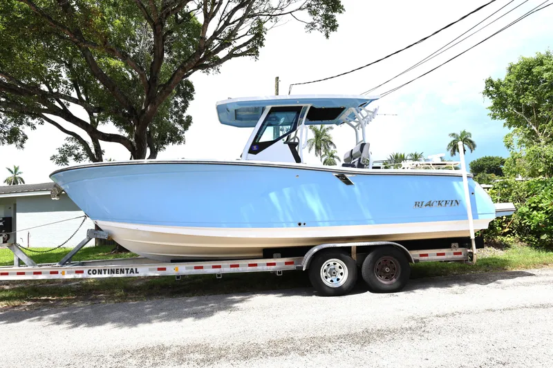 Slide: The Image of 2021 Blackfin 272 CC boat on trailer, parked outdoors under trees. - 1