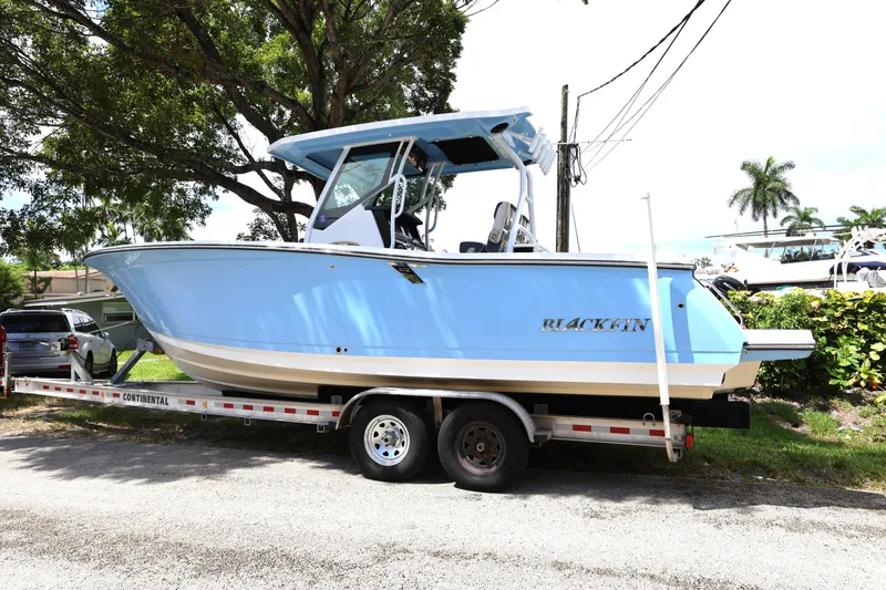 Slide: The Image of 2021 Blackfin 272 CC boat on trailer, parked outdoors under trees. - 2