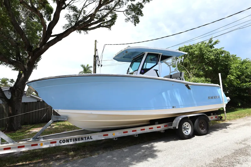 Slide: The Image of 2021 Blackfin 272 CC boat on trailer, parked outdoors under trees. - 3