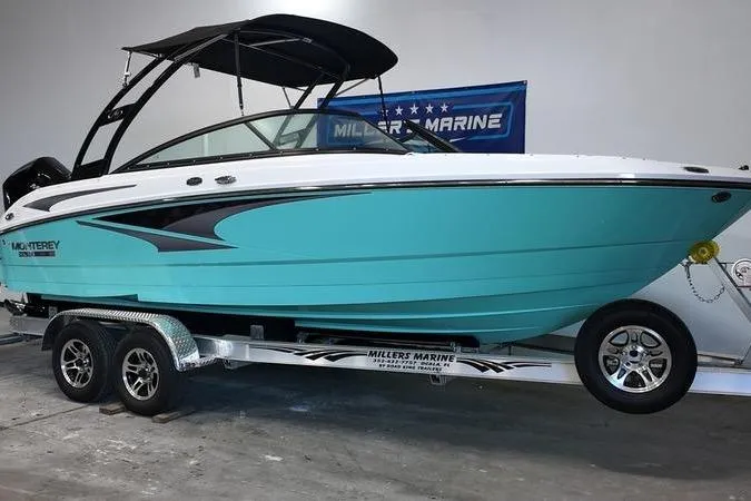 Slide: The Image of 2024 Monterey M-225 boat on trailer, turquoise hull, displayed indoors at Miller's Marine. - 0