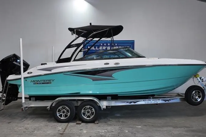 Slide: The Image of 2024 Monterey M-225 boat in turquoise on trailer, displayed indoors. - 1