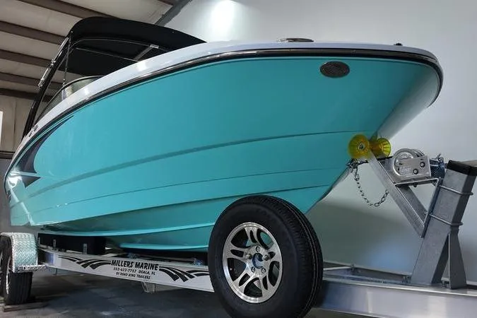 Slide: The Image of 2024 Monterey M-225 boat in turquoise on a trailer, displayed indoors. - 2