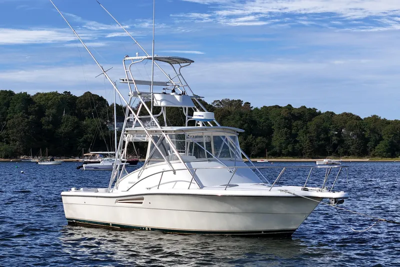 The Image of 2003 Pursuit 3000 Offshore boat anchored on a serene lake with forested shoreline. - 0