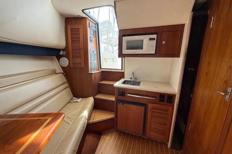 Slide: The Image of 2003 Pursuit 3000 Offshore boat interior with kitchenette, seating, and wood accents. - 19