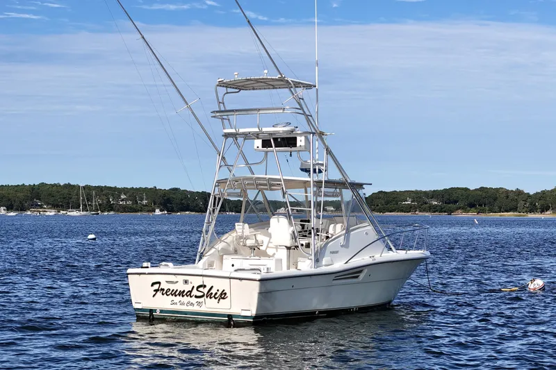 Slide: The Image of 2003 Pursuit 3000 Offshore boat anchored on calm water with scenic shoreline background. - 3