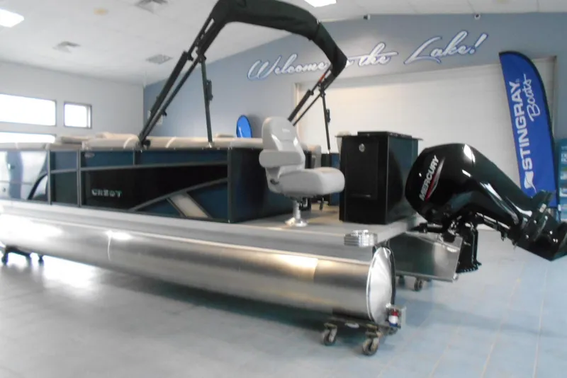Slide: The Image of 2025 Crest Classic Fish 220 pontoon boat displayed indoors with Mercury outboard motor. - 4