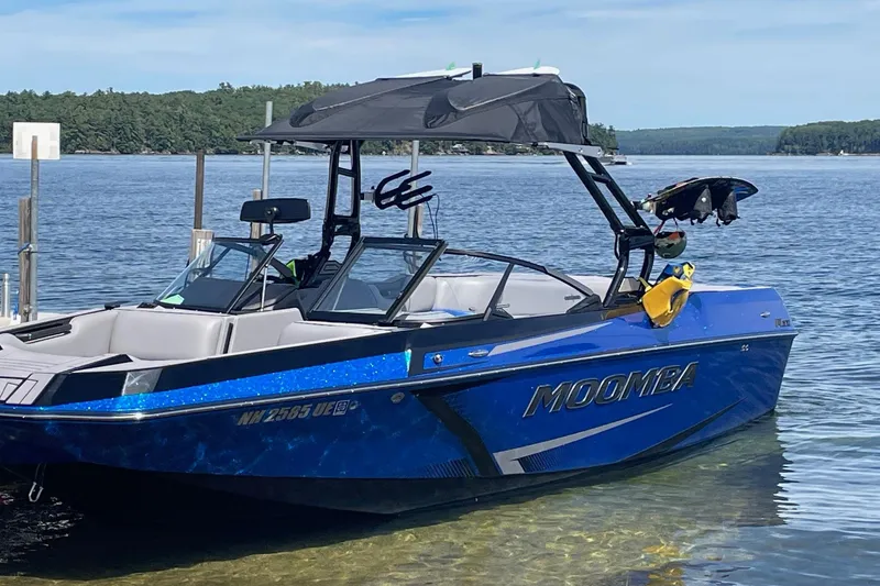 Slide: The Image of 2023 Moomba Max boat in blue, docked on a serene lake with lush greenery. - 14