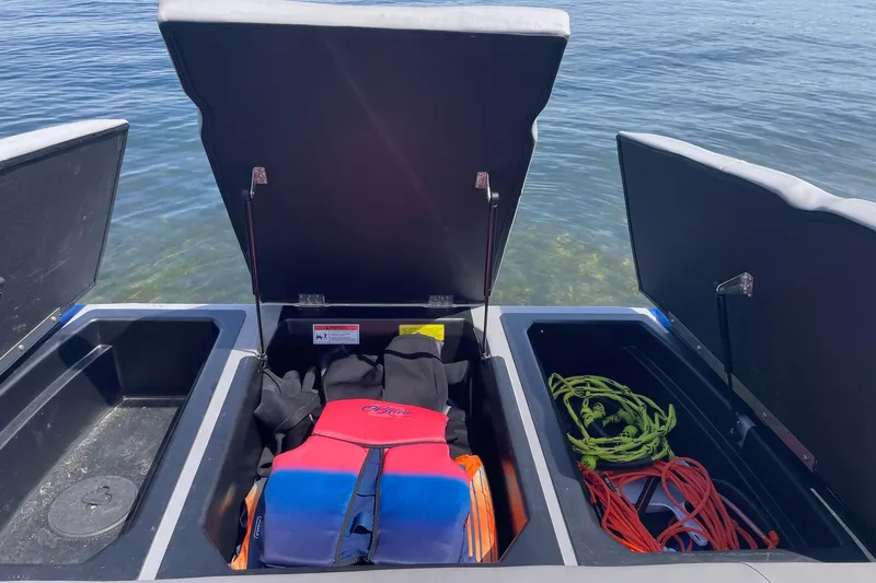 Slide: The Image of 2023 Moomba Max boat storage compartments with life jacket and ropes by the water. - 15