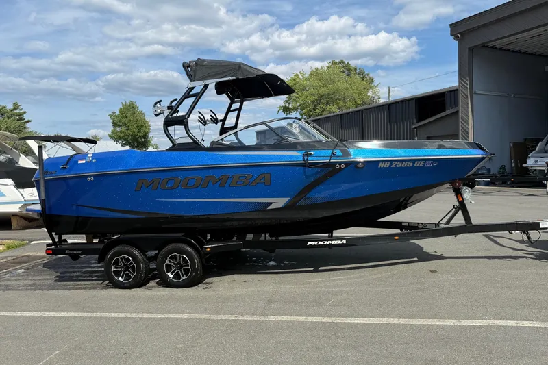 Slide: The Image of 2023 Moomba Max boat in vibrant blue on a trailer, parked outdoors. - 2