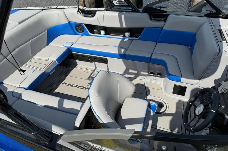 Slide: The Image of 2023 Moomba Max boat interior with blue and gray seating, steering wheel, and cup holders. - 7
