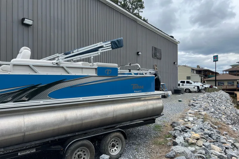 Slide: The Image of 2021 Tahoe Pontoon GT Center Console Fish 25' on trailer near building and rocky shoreline. - 1