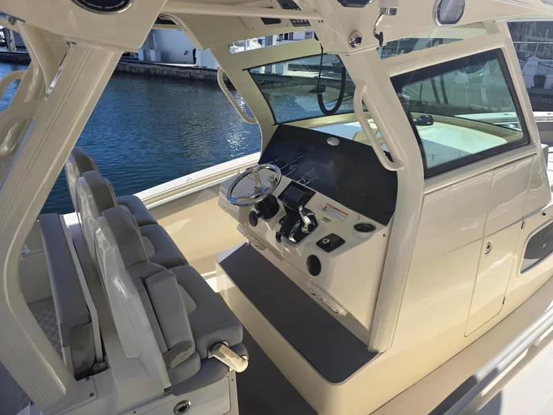 Slide: The Image of 2024 Scout 355 LXF boat interior with helm and seating, docked by the water. - 19
