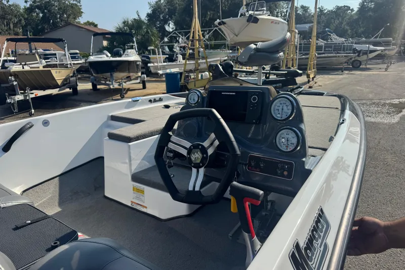 Slide: The Image of 2021 Bass Cat Margay boat interior with steering wheel and dashboard, parked among other boats. - 20