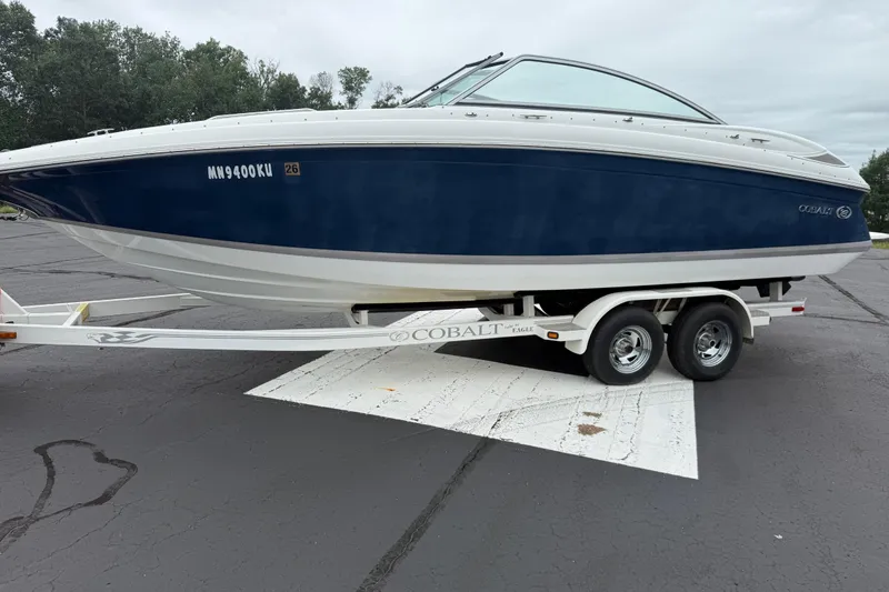 Slide: The Image of 2007 Cobalt 232 boat on trailer, parked on asphalt, with trees in the background. - 8