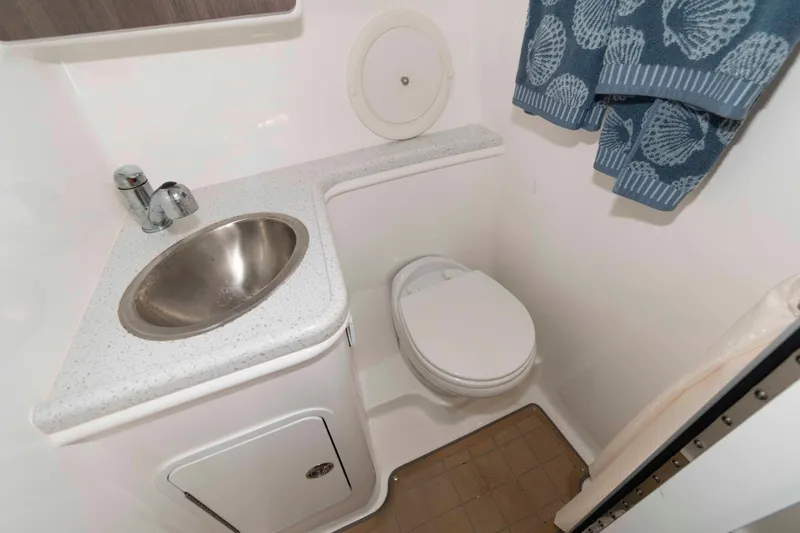 Slide: The Image of 2019 Rinker 290 EX boat bathroom with sink, toilet, and blue seashell towel. - 9