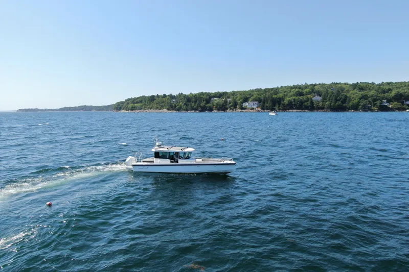 Slide: The Image of 2020 Axopar 28 Cabin Aft Cabin cruising on a scenic, blue ocean near a forested coastline. - 5