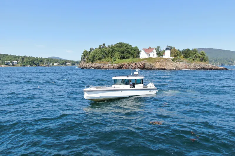 Slide: The Image of 2020 Axopar 28 Cabin Aft Cabin boat cruising near a scenic island with lighthouse. - 6