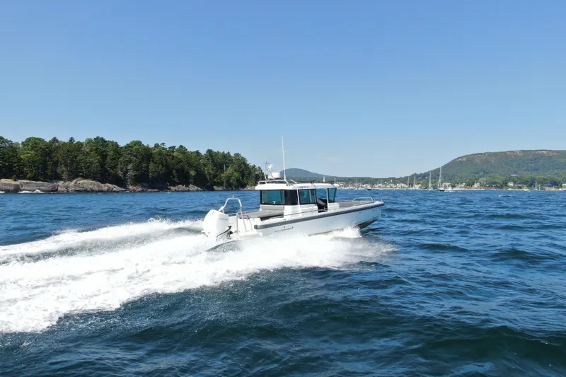 Slide: The Image of 2020 Axopar 28 Cabin Aft Cabin cruising on a scenic lake with forested shoreline. - 8