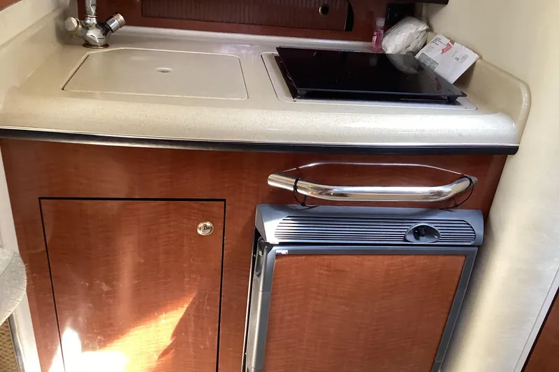 Slide: The Image of 2004 Sea Ray 280 Sundancer galley with sink, stove, and compact fridge. - 10