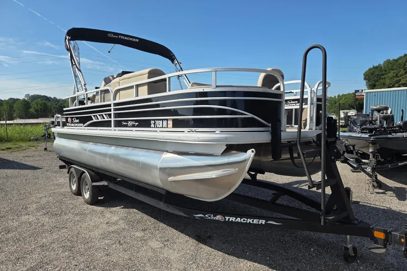 Slide: The Image of 2021 Sun Tracker Fishin' Barge 20 DLX pontoon boat on trailer, parked outdoors. - 2