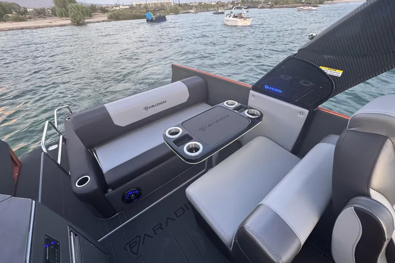 Slide: The Image of 2026 Paradigm 236 Surf boat interior with seating and cup holders on a lake. - 8
