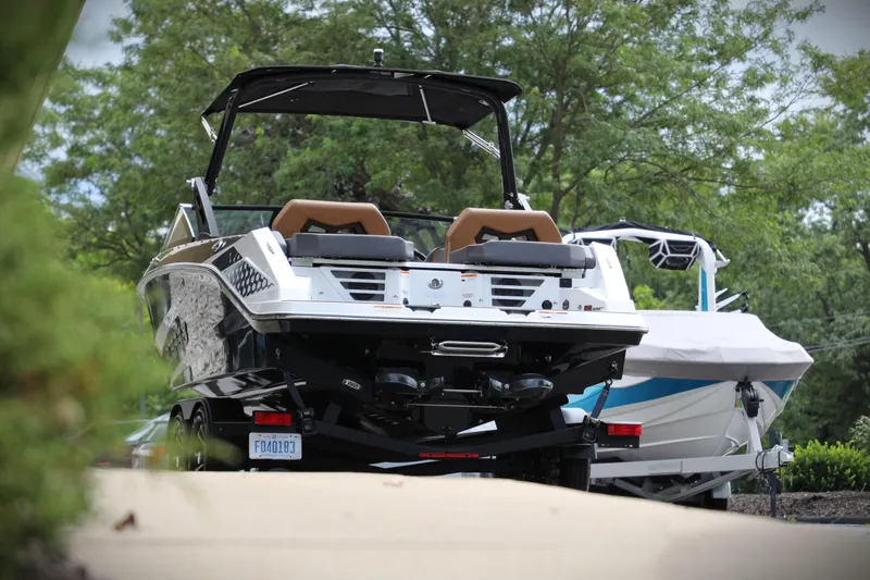 Slide: The Image of 2024 Scarab 235 Wake ID boat on trailer, parked outdoors with trees in background. - 16