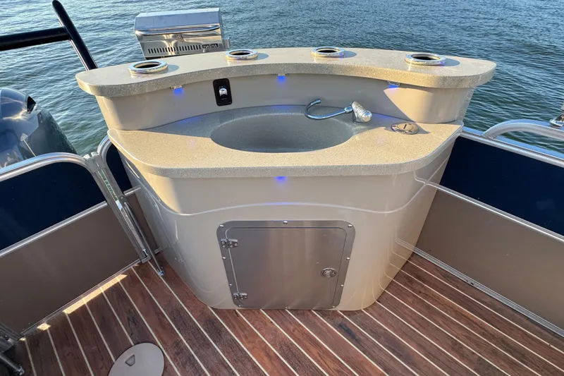 Slide: The Image of Outdoor bar sink on 2016 Xcursion 23RFE boat, featuring wooden deck and water backdrop. - 17