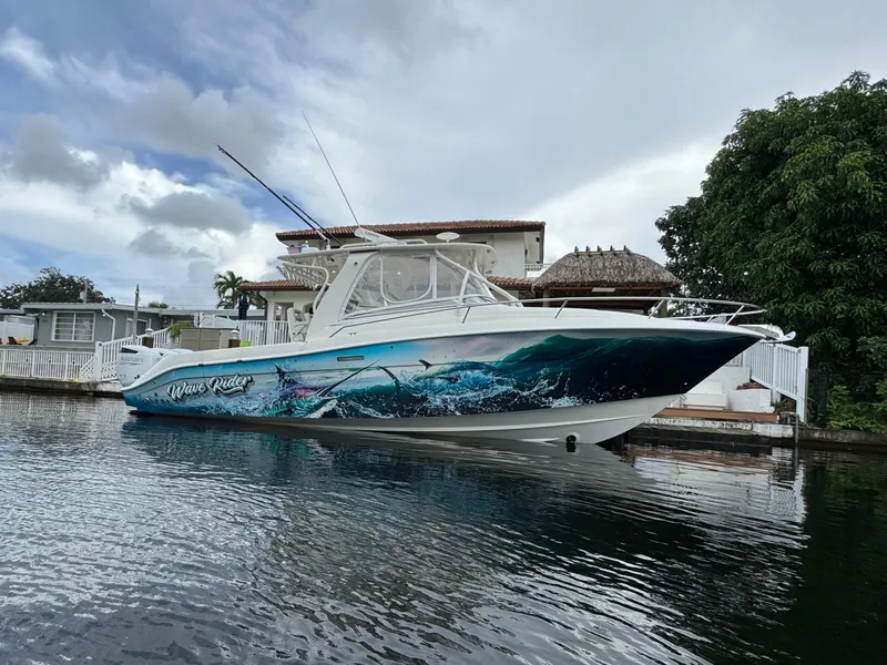 Slide: The Image of 2010 Hydra-Sports 3500 VX boat with vibrant ocean-themed hull design docked by a house. - 2
