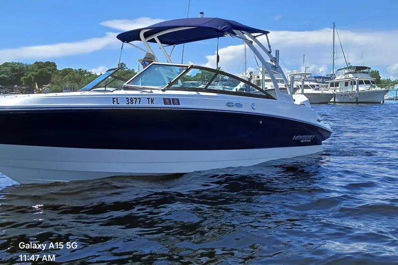 Slide: The Image of 2023 Monterey 225 boat on water with blue canopy, docked near other vessels. - 3