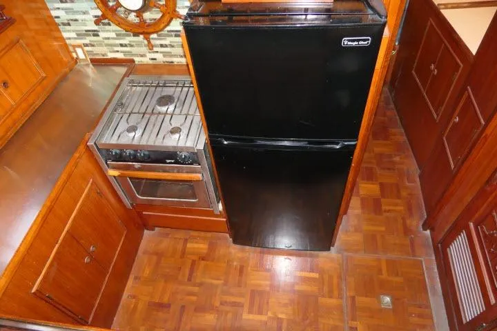 Slide: The Image of 1983 CHB 45 yacht kitchen with stove, black fridge, and wooden cabinetry. - 16