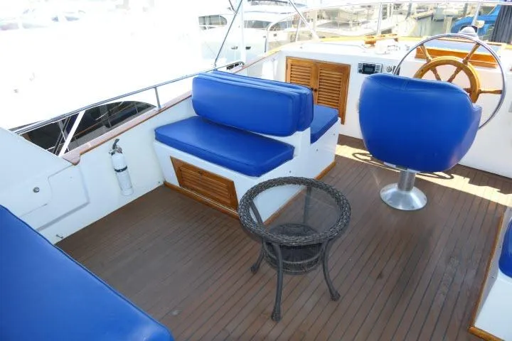 Slide: The Image of 1983 CHB 45 yacht deck with blue seating, wicker table, and wooden steering wheel. - 54