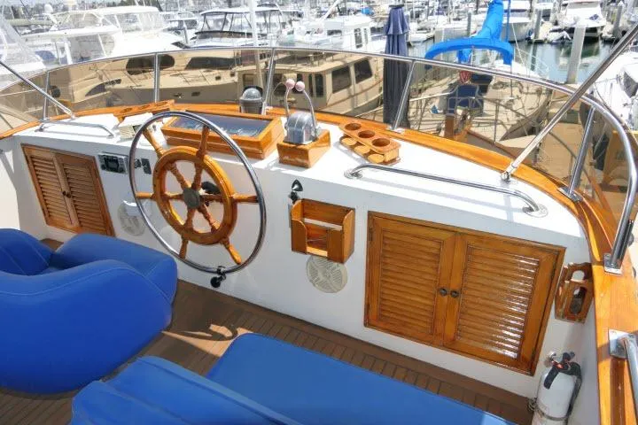 Slide: The Image of 1983 CHB 45 yacht helm with wooden wheel, blue seating, and marina background. - 58