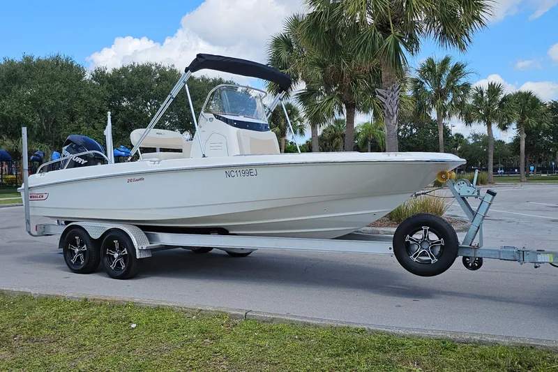 Slide: The Image of 2018 Boston Whaler 210 Dauntless boat on trailer, parked near palm trees. - 7