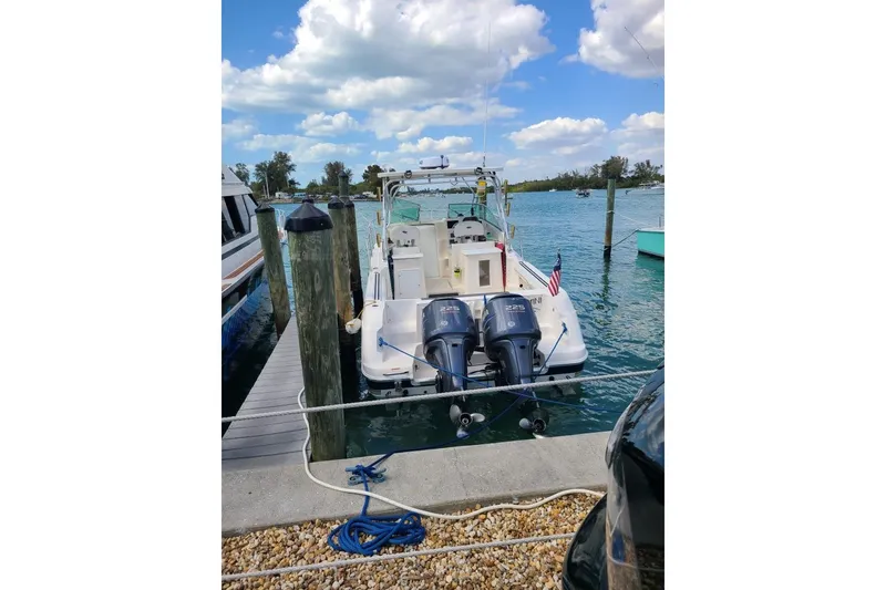 Slide: The Image of 2005 Aquasport 275 Explorer docked with dual outboard engines, clear sky, and calm water. - 1