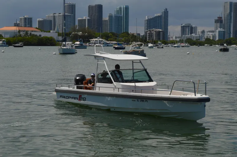 Slide: The Image of 2015 Axopar T-Top boat cruising in a marina with city skyline background. - 2