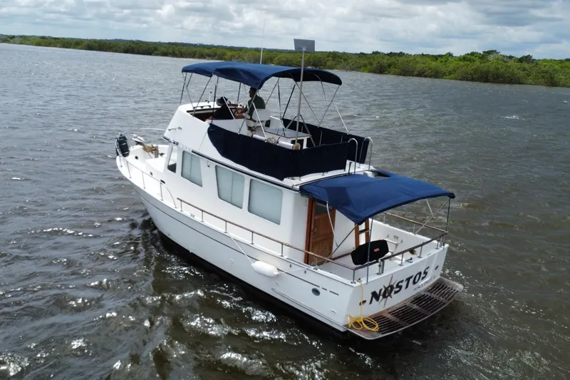 Slide: The Image of 1973 CHB 34 boat cruising on a river with blue canopies and lush green shoreline. - 2