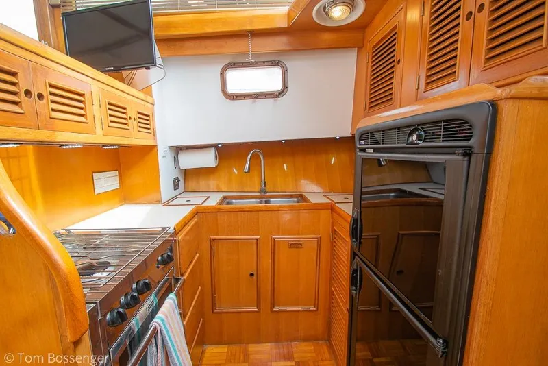 Slide: The Image of 1986 Ponderosa 47 yacht kitchen with wooden cabinetry, stove, sink, and compact refrigerator. - 14