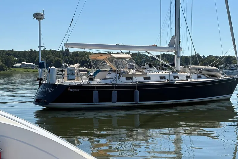 Slide: The Image of 2005 Tartan 4100 sailboat docked on calm water, surrounded by lush greenery. - 2