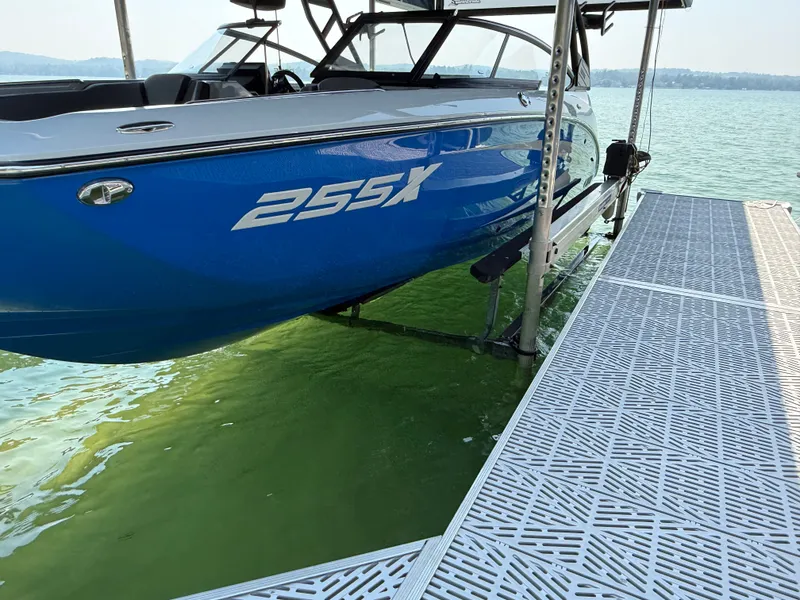 The Image of 2025 Yamaha Boats 255 XD in blue on a serene lake, surrounded by lush greenery. - 0