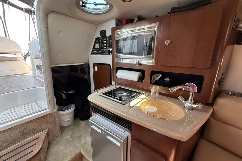 Slide: The Image of 2016 Crownline 264 CR boat interior with kitchenette, featuring sink, stove, and microwave. - 18