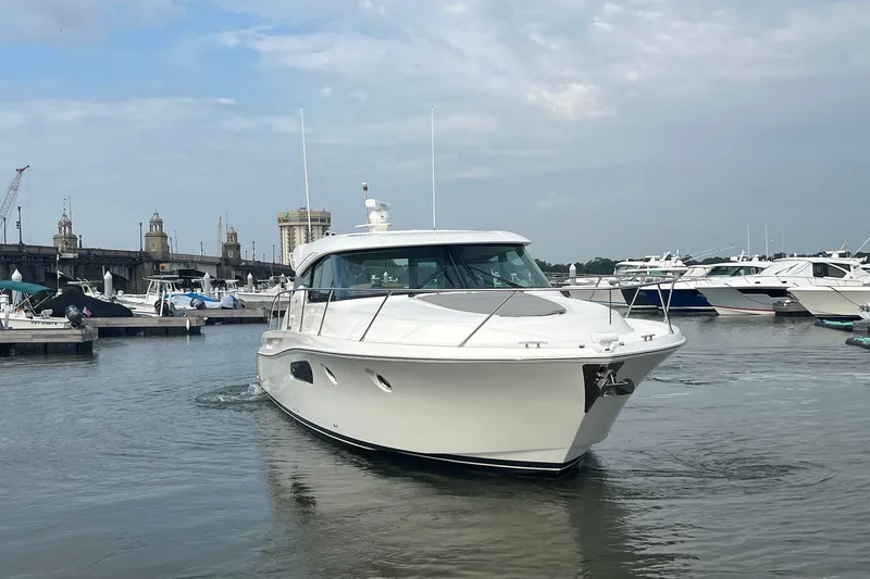 Slide: The Image of 2023 Tiara Yachts C44 Coupe in marina, surrounded by other boats, under cloudy sky. - 10