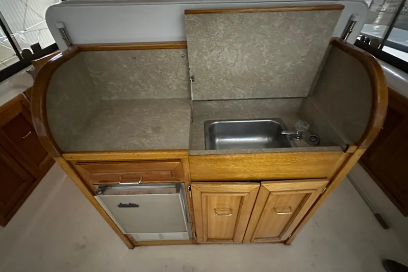 Slide: The Image of 1982 Egg Harbor 42 Flybridge Motoryacht galley with sink, wooden cabinetry, and compact fridge. - 31