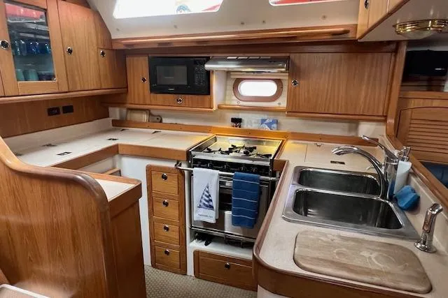 Slide: The Image of Interior of 2003 Catalina 470 Sloop, featuring a well-equipped kitchen with wooden cabinetry. - 2
