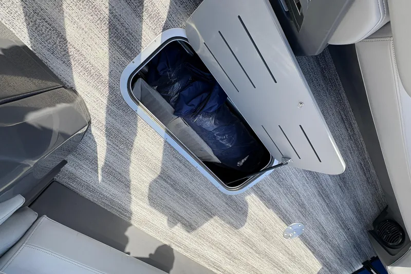 Slide: The Image of 2026 Bennington 26 MCSB boat storage compartment with open lid, revealing interior contents. - 12
