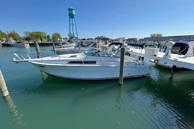 Slide: The Image of 1991 Four Winns 325 Express Vista boat docked in a marina with a water tower. - 1