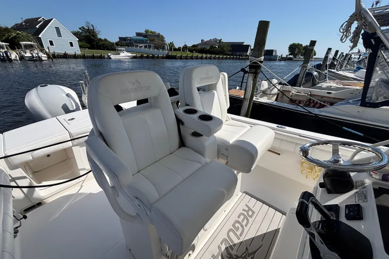 Slide: The Image of 2017 Regulator 28 boat interior with white seating and steering wheel, docked by waterfront homes. - 32