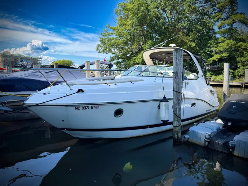 Slide: The Image of 2016 Rinker 290 Express boat docked in a marina, surrounded by trees and clear skies. - 1